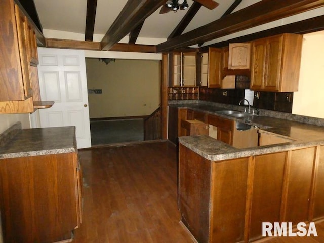 kitchen with vaulted ceiling with beams, a peninsula, dark wood-type flooring, a sink, and brown cabinetry