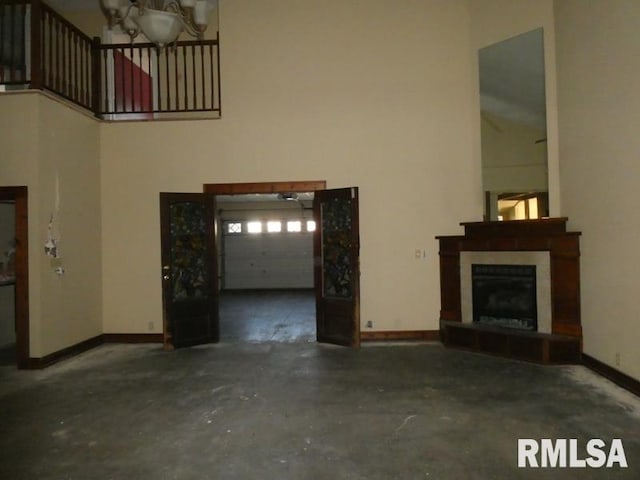 unfurnished living room with a fireplace with raised hearth, concrete floors, a towering ceiling, and baseboards