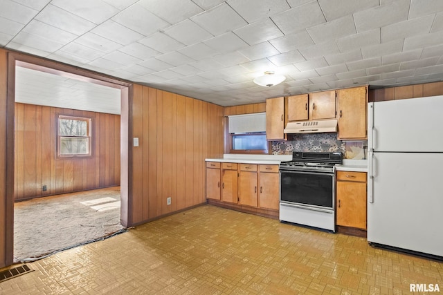 kitchen featuring wooden walls, decorative backsplash, white refrigerator, and stove