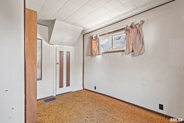 carpeted spare room featuring wooden walls