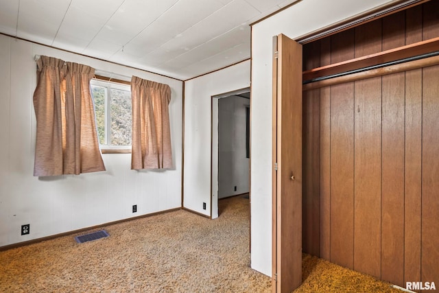 unfurnished bedroom with light carpet, a closet, and wood walls