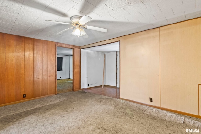 carpeted spare room with wood walls and ceiling fan