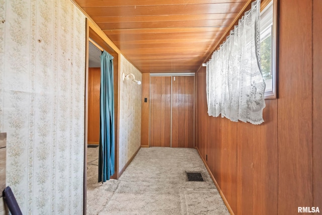 hallway with wooden walls, wood ceiling, and light colored carpet