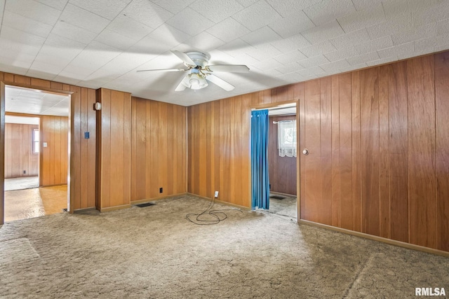 spare room with ceiling fan, wood walls, and carpet flooring