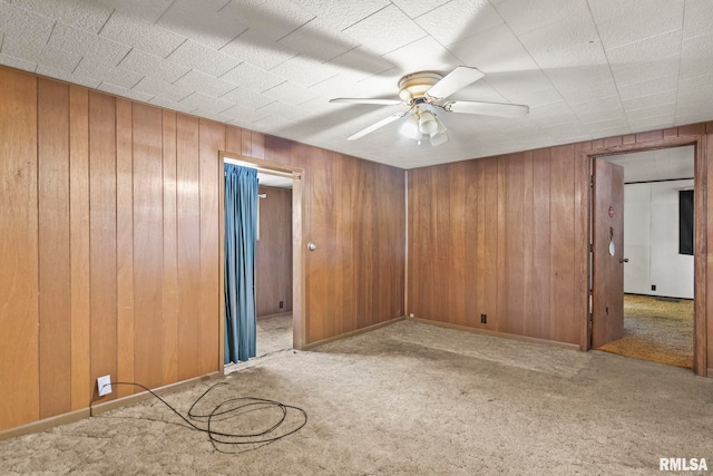 carpeted empty room featuring ceiling fan and wooden walls