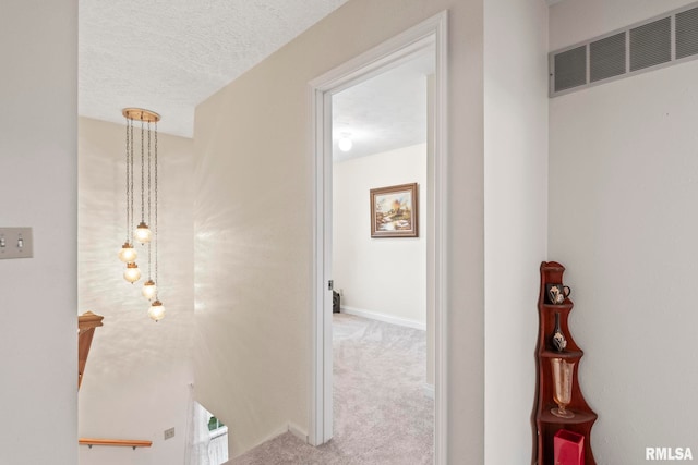 corridor featuring a textured ceiling and light colored carpet