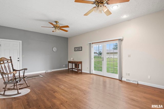 living area with hardwood / wood-style flooring, a textured ceiling, and ceiling fan