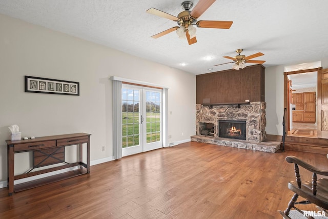 living room featuring a stone fireplace, hardwood / wood-style floors, ceiling fan, and a textured ceiling