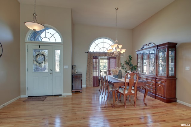 dining space with high vaulted ceiling, a wealth of natural light, a notable chandelier, and light hardwood / wood-style flooring