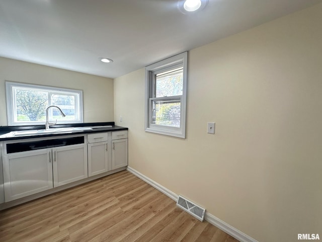 kitchen featuring light hardwood / wood-style flooring, white cabinetry, sink, and a wealth of natural light