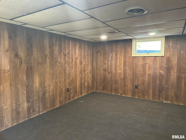 basement with a drop ceiling, wood walls, and dark carpet