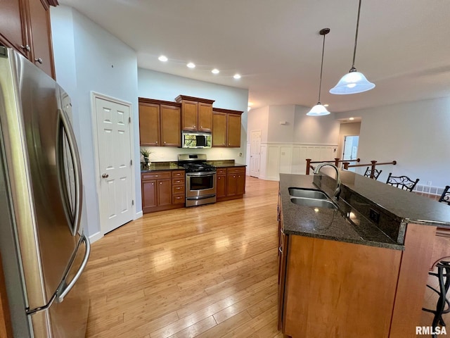 kitchen with appliances with stainless steel finishes, sink, a kitchen bar, light wood-type flooring, and decorative light fixtures