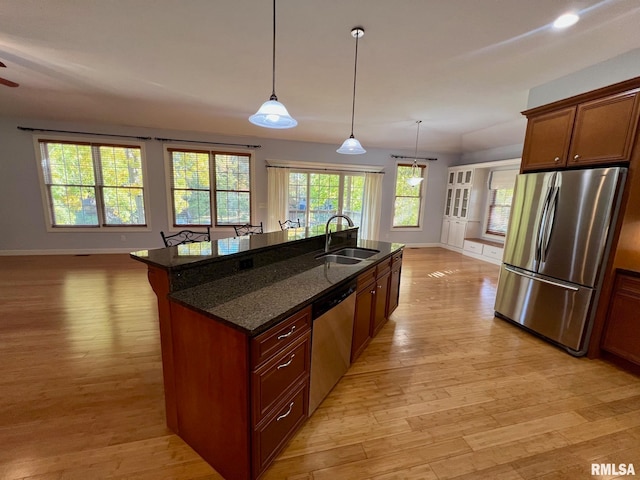 kitchen featuring stainless steel appliances, dark stone counters, a center island with sink, sink, and light hardwood / wood-style floors