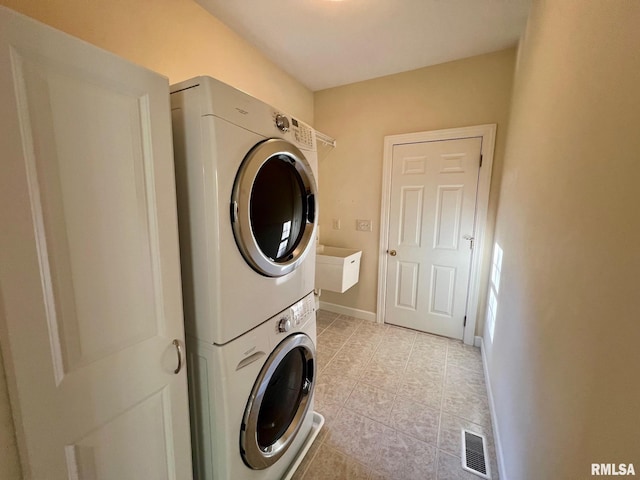 clothes washing area with sink, stacked washer / dryer, and light tile patterned floors