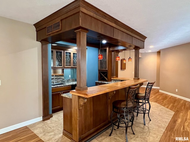 bar with sink, ornate columns, and light wood-type flooring