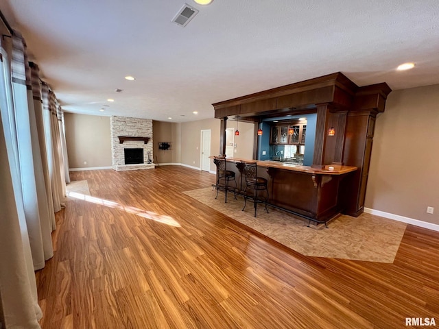 bar with a stone fireplace, a textured ceiling, and light hardwood / wood-style flooring