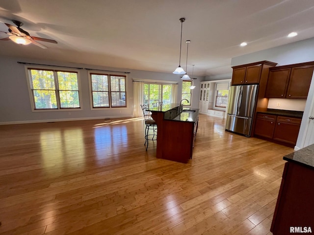 kitchen with an island with sink, a breakfast bar, stainless steel refrigerator, light hardwood / wood-style flooring, and decorative light fixtures