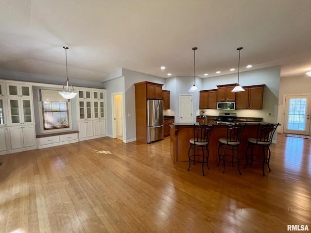 kitchen featuring appliances with stainless steel finishes, light hardwood / wood-style flooring, pendant lighting, and a kitchen breakfast bar