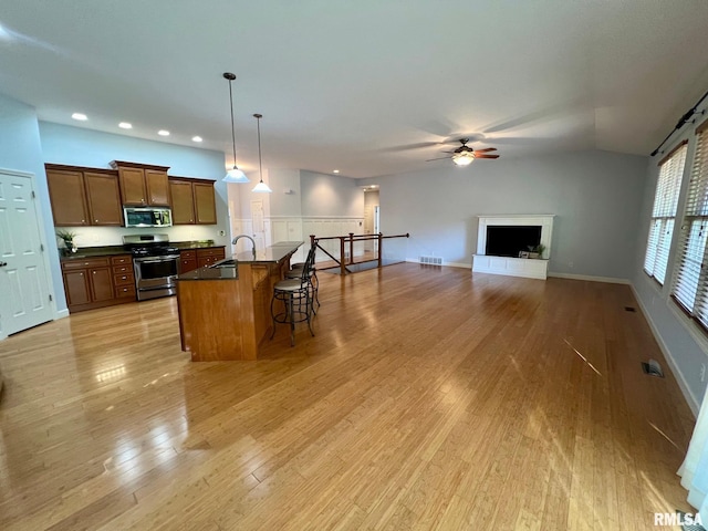 kitchen with a kitchen bar, stainless steel appliances, pendant lighting, light hardwood / wood-style flooring, and a kitchen island with sink