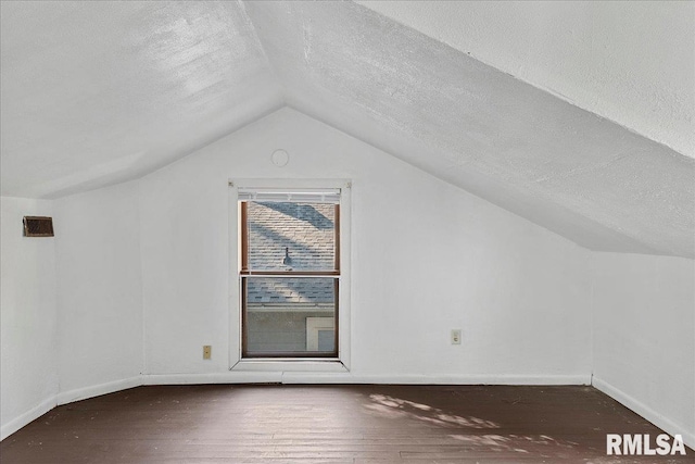 additional living space featuring dark hardwood / wood-style floors, vaulted ceiling, and a textured ceiling