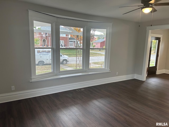 empty room with a wealth of natural light, dark wood-type flooring, and ceiling fan