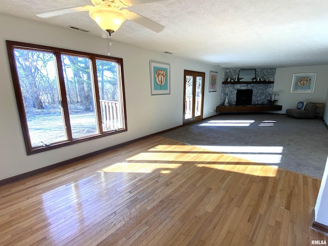 unfurnished living room featuring ceiling fan, a fireplace, a textured ceiling, and light wood-type flooring