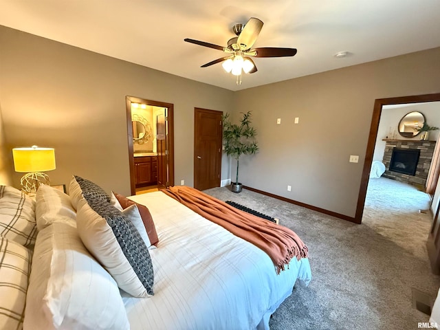 carpeted bedroom with ensuite bathroom, a stone fireplace, and ceiling fan