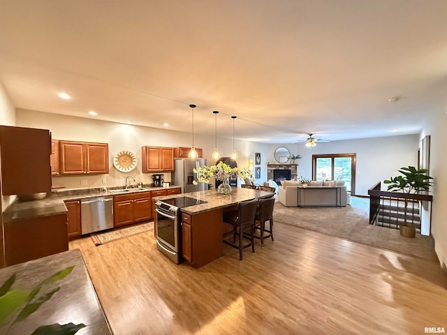 kitchen with a kitchen breakfast bar, a center island, stainless steel appliances, a stone fireplace, and decorative light fixtures