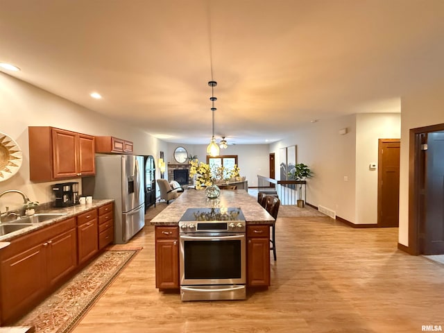 kitchen featuring a kitchen island, hanging light fixtures, sink, appliances with stainless steel finishes, and light hardwood / wood-style floors