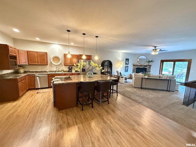 kitchen with a breakfast bar area, hanging light fixtures, light wood-type flooring, appliances with stainless steel finishes, and a fireplace