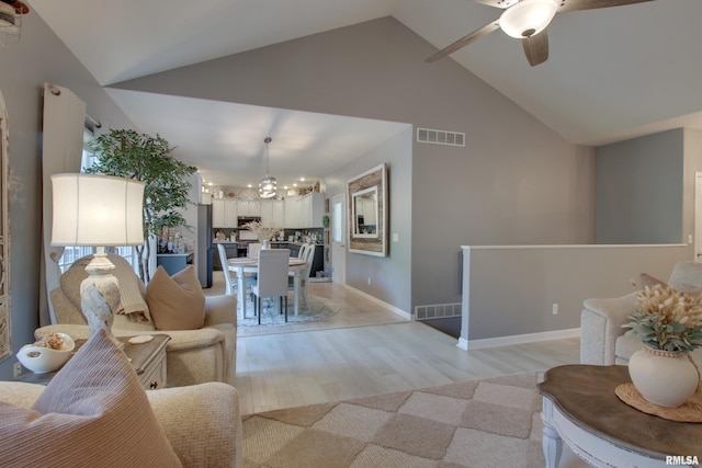 living room with high vaulted ceiling, light hardwood / wood-style flooring, and ceiling fan with notable chandelier