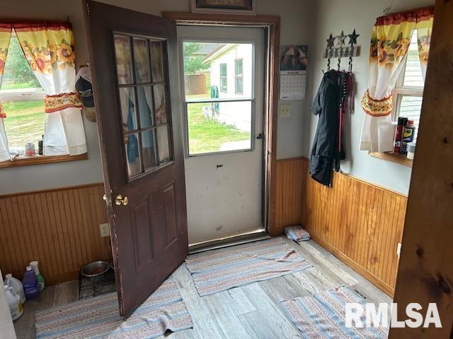 doorway to outside with a wainscoted wall, plenty of natural light, wooden walls, and light wood finished floors