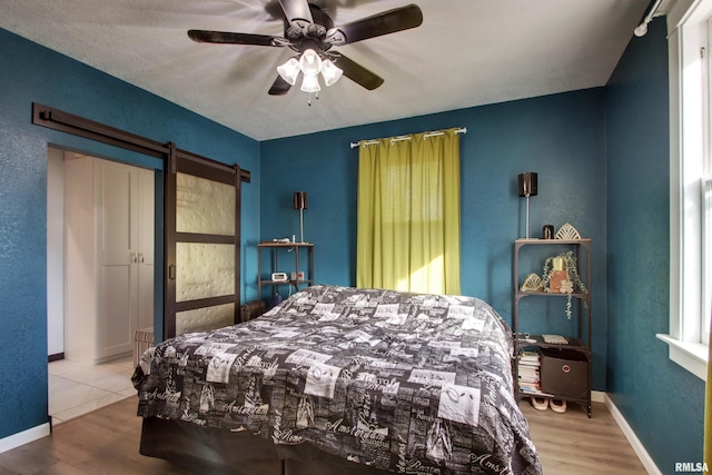 bedroom featuring a barn door, multiple windows, hardwood / wood-style flooring, and ceiling fan