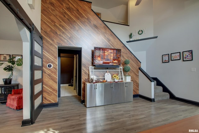 interior space with a towering ceiling, wood walls, a barn door, and wood-type flooring