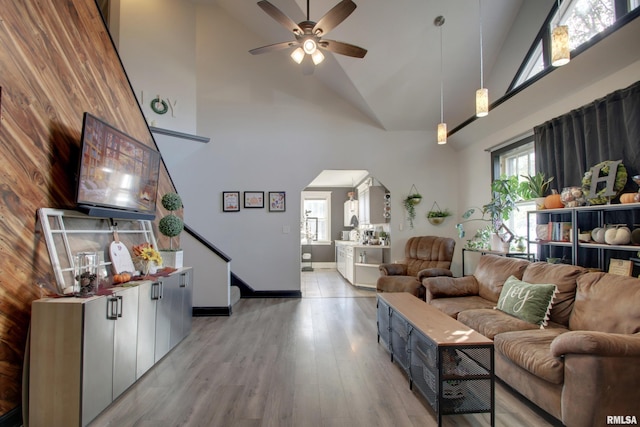 living room featuring light hardwood / wood-style floors, high vaulted ceiling, wooden walls, and ceiling fan