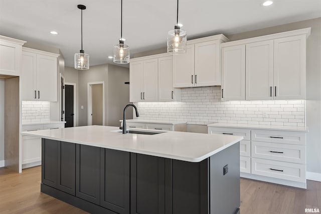 kitchen with pendant lighting, light wood-type flooring, white cabinetry, and sink