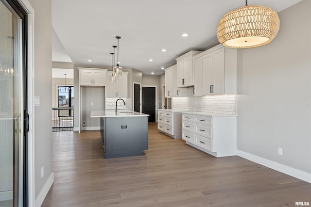 kitchen with white cabinetry, sink, pendant lighting, light hardwood / wood-style floors, and a kitchen island with sink