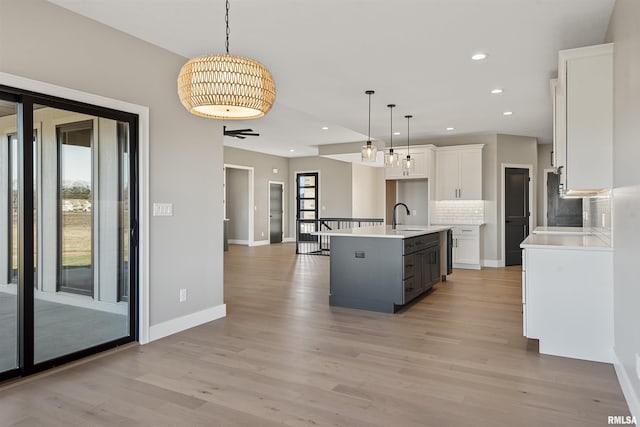 kitchen with pendant lighting, light hardwood / wood-style floors, white cabinetry, and an island with sink