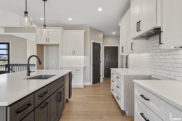 kitchen featuring sink, decorative backsplash, light wood-type flooring, decorative light fixtures, and white cabinetry