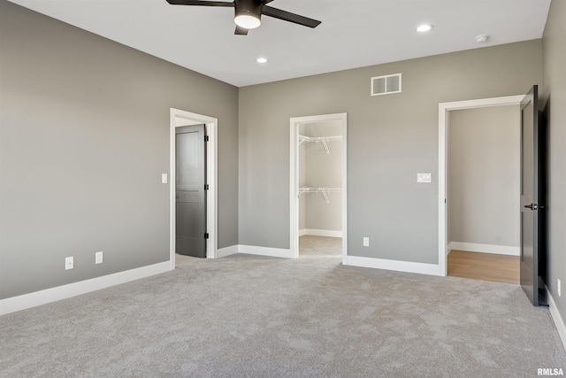 unfurnished bedroom featuring a spacious closet, a closet, ceiling fan, and light carpet