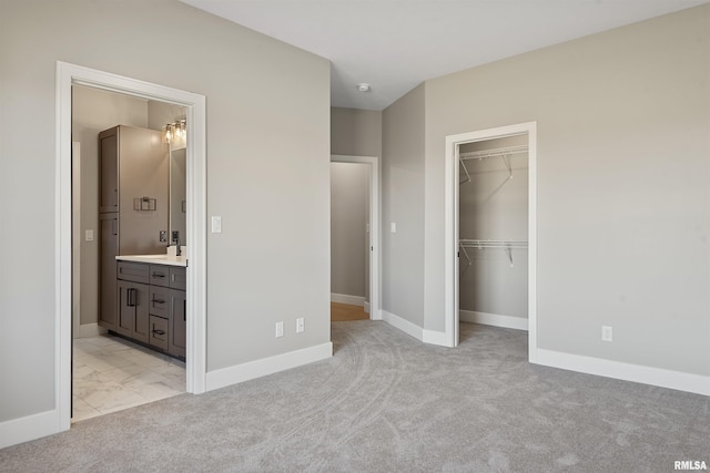 unfurnished bedroom featuring a walk in closet, ensuite bathroom, a closet, and light carpet