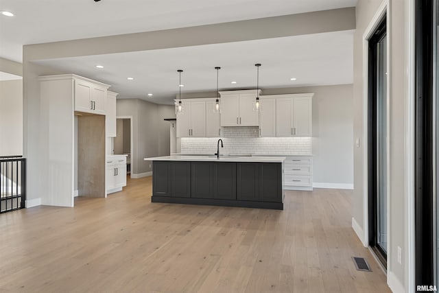 kitchen with white cabinetry, a kitchen island with sink, hanging light fixtures, and light hardwood / wood-style flooring