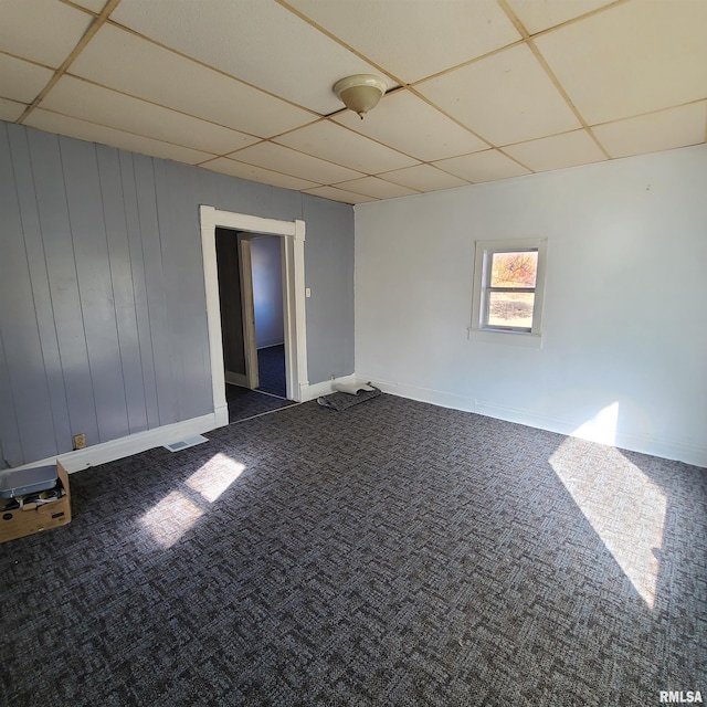 unfurnished room with a paneled ceiling and dark colored carpet