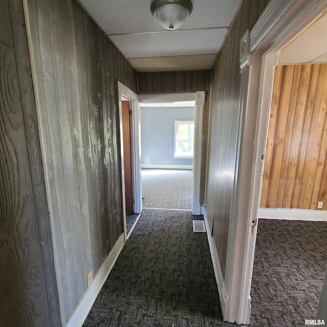 hallway with wooden walls and dark colored carpet