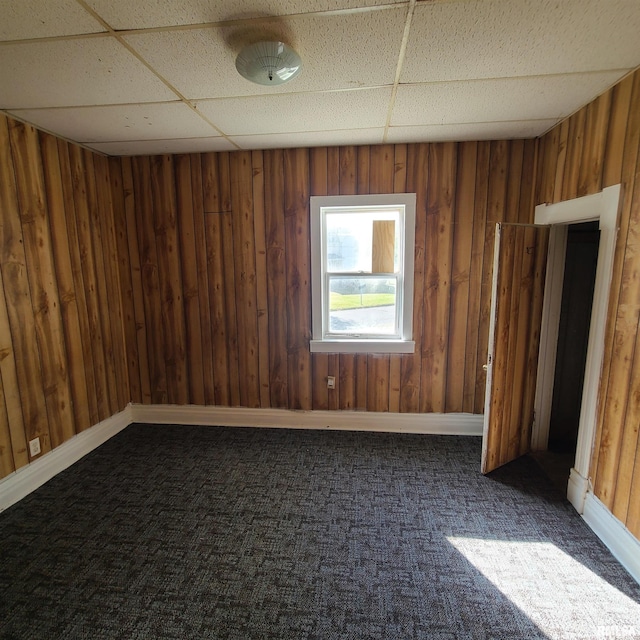 carpeted empty room with a drop ceiling and wooden walls