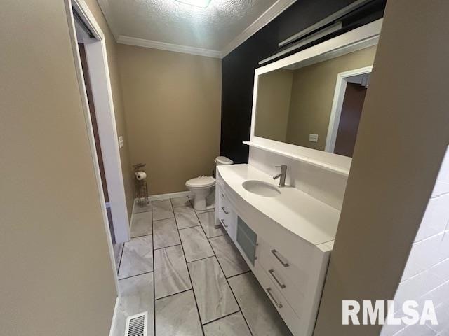 bathroom with toilet, vanity, a textured ceiling, and ornamental molding