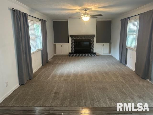 unfurnished living room featuring a fireplace, carpet floors, ceiling fan, and crown molding