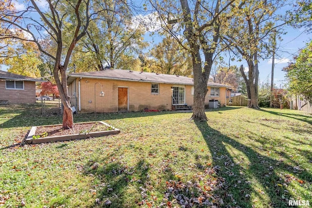 rear view of house with a lawn, a garden, fence, and entry steps