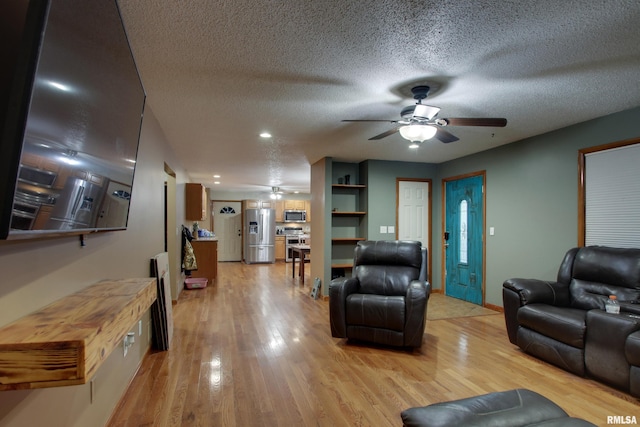 living room featuring ceiling fan, a textured ceiling, and light wood-type flooring