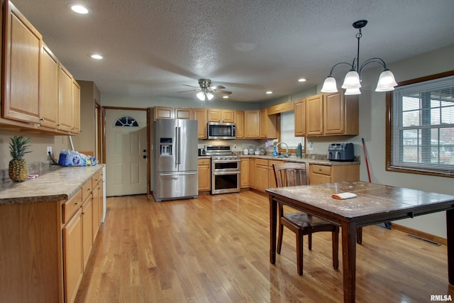 kitchen featuring stainless steel appliances, light hardwood / wood-style floors, sink, ceiling fan, and pendant lighting